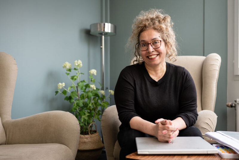 En leende kvinna sitter i en fåtölj och har händerna på ett bord