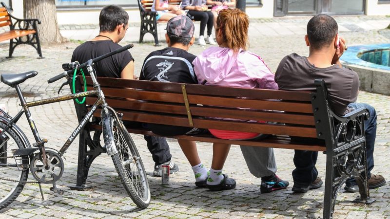 fyra ungdomar bakifrån om sitter på en torgbänk