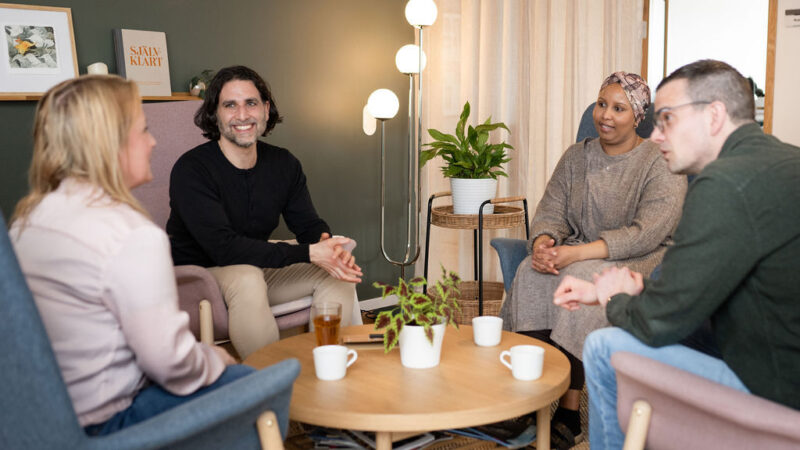 Fyra personer sitter i fåtöljer runt ett bord