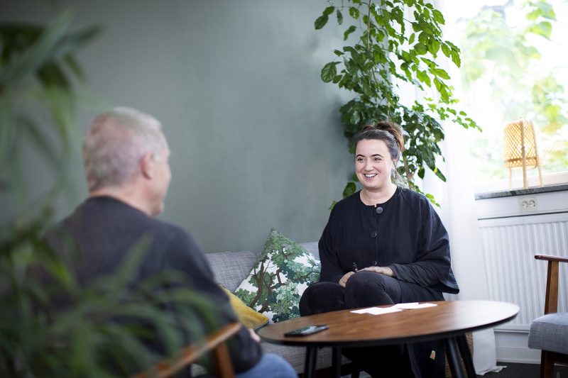 En man och en kvinna  sitter mittemot varandra och samtalar. Gröna växter i bakgrunden