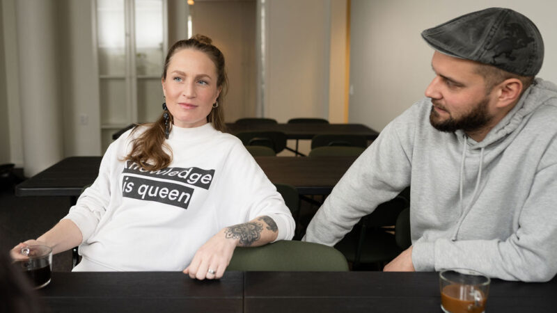 En person med keps, en person med vit college tröja och taturering på armen