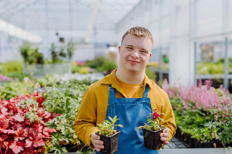 En kille med down syndrom står bland plantor i ett växthus
