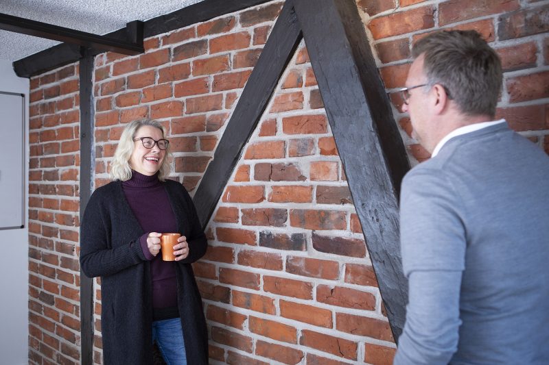 En kvinna och en man står och samtalar framför en gammal tegelvägg