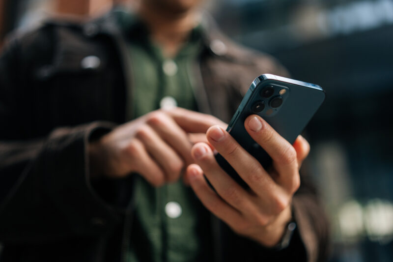 Händerna på en person som håller i en mobiltelefon och skriver på den med ett finger