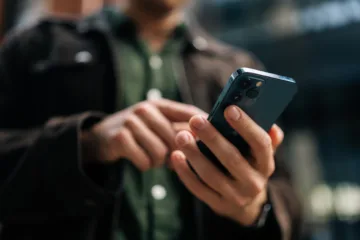 Händerna på en person som håller i en mobiltelefon och skriver på den med ett finger